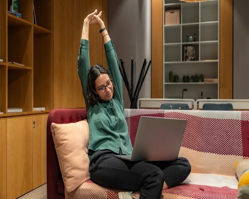 A person taking a break from laptop, stretching arms inside a cozy home workspace
